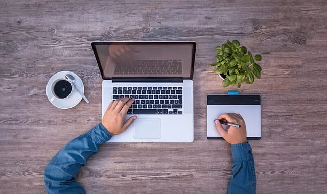 Overhead view of workspace with laptop, tablet, coffee, and plant.