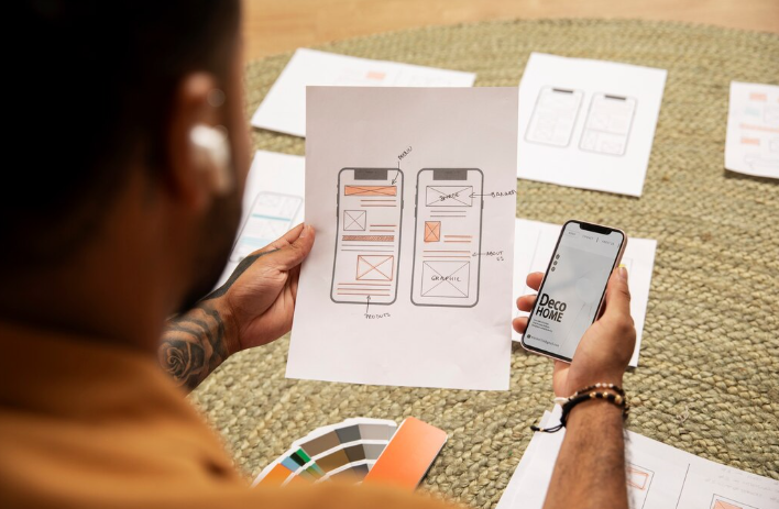 A person holding a printed mobile app wireframe while checking a phone displaying.