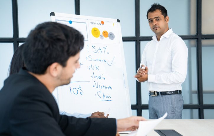 Businessman presenting data and statistics on whiteboard during meeting.