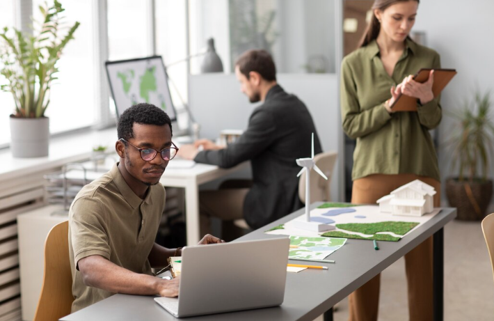 Man working on laptop in eco-friendly office with wind model.