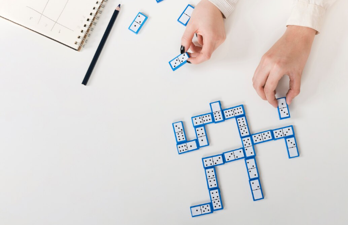 Hands arranging domino tiles into structured puzzle pattern on table.