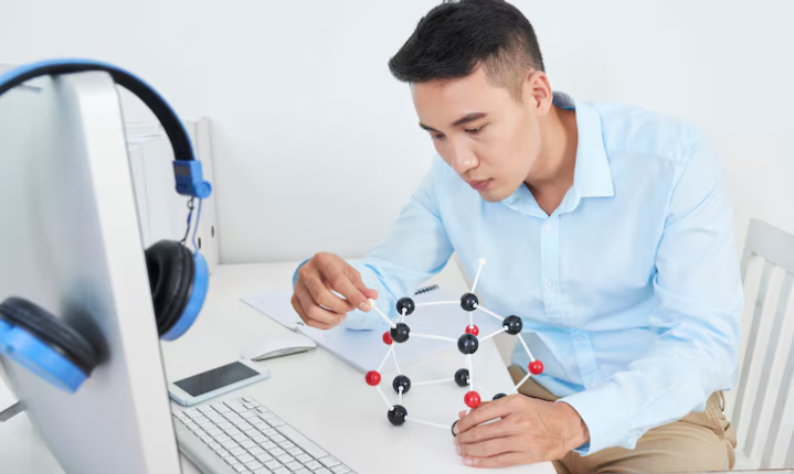 Focused man assembling molecular model while working at computer desk.