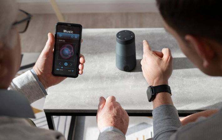 Two men using a smartphone to control a smart speaker.