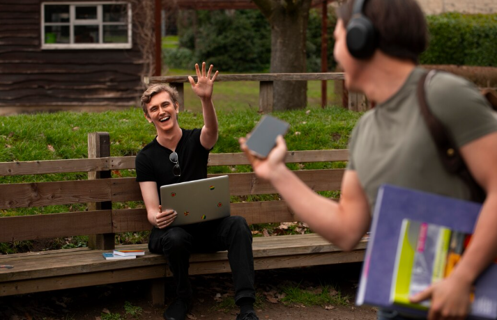 Person waving while using laptop outdoors.