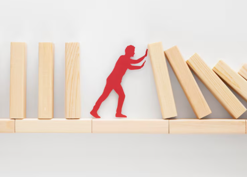 Alt text: Red figure stopping falling wooden blocks from collapsing.