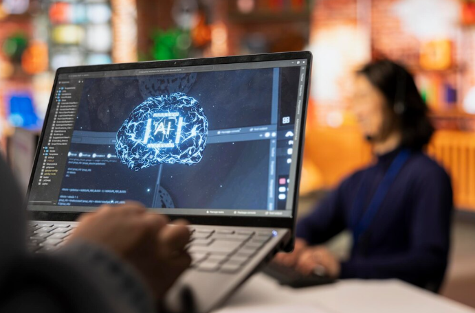 Person holding a laptop showing an AI brain graphic on the screen, with another person blurred in the background.