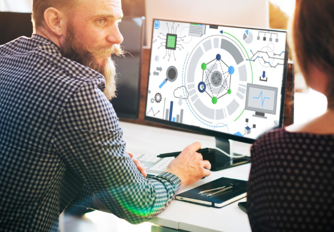 A man presenting automation concepts on a computer screen to a colleague in a modern office setting.