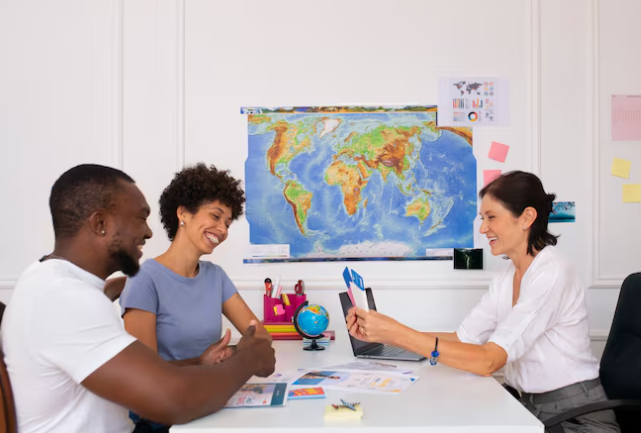 A travel agent consulting with two clients at a desk, with a world map on the wall in the background.