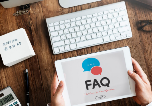 Hands holding tablet showing FAQ page on office desk.