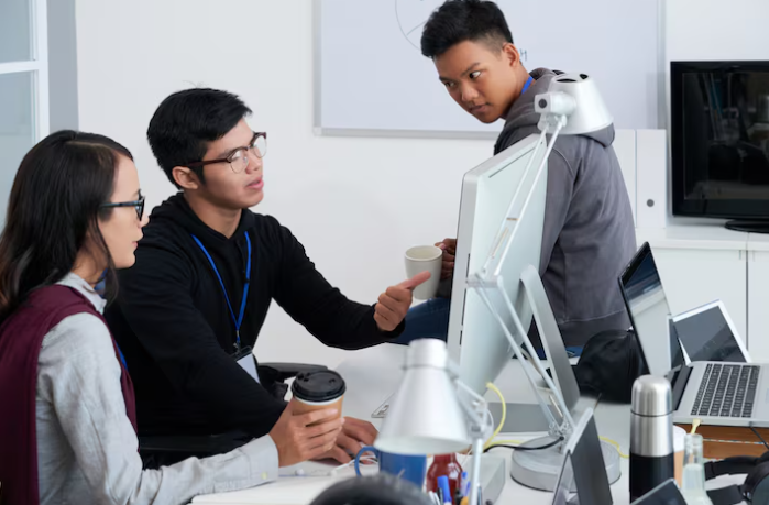 Team of developers discussing project details around desktop computer.