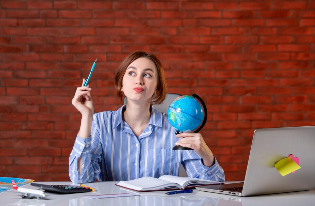 Thoughtful woman holding globe, planning travel at her desk.