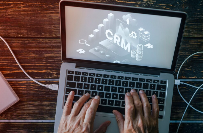 Hands typing on laptop with CRM system displayed on screen.