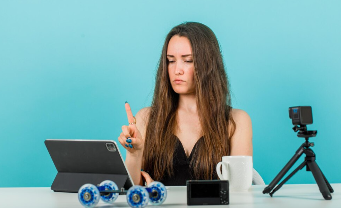 Focused woman operating tablet with gadgets and camera on desk.