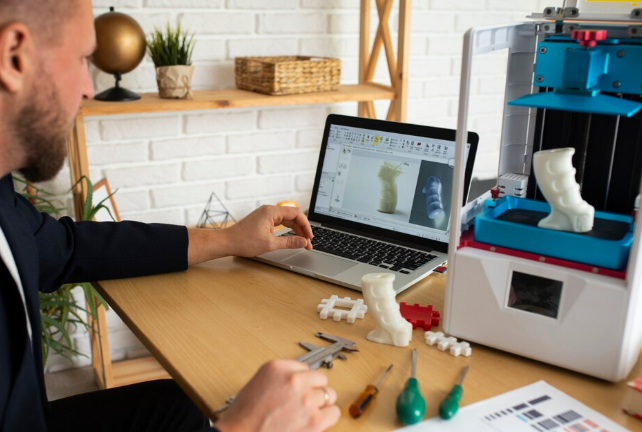 Designer working on 3D modeling project beside a 3D printer.