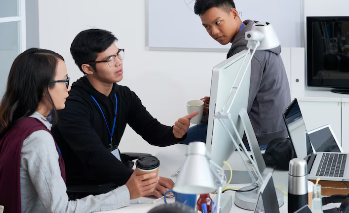 Group of young professionals discussing work beside computer and robot.