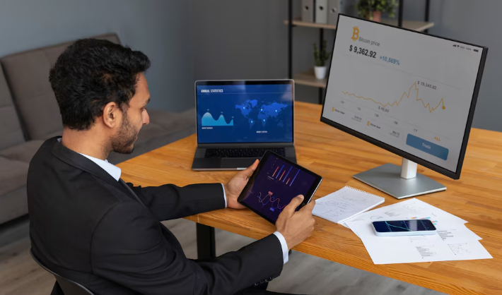 Businessman reviewing financial dashboards on tablet and monitors.