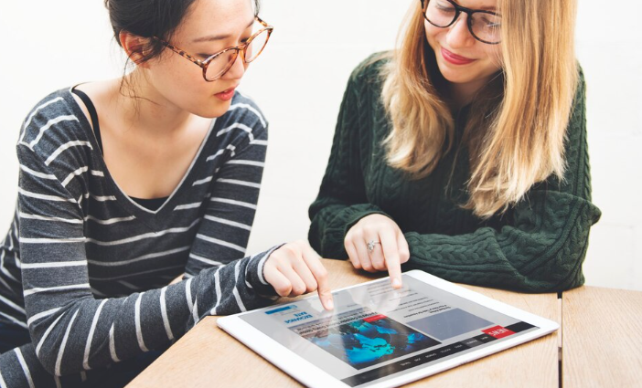 Two young women discussing content while pointing at a digital tablet.