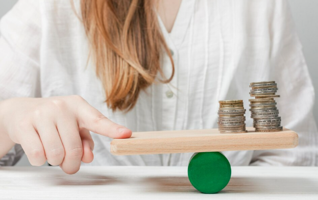 Hand balancing stacked coins on wooden seesaw representing financial stability concept.