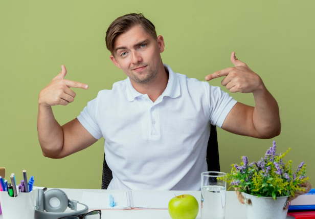 Confident young man in white shirt pointing at himself proudly.
