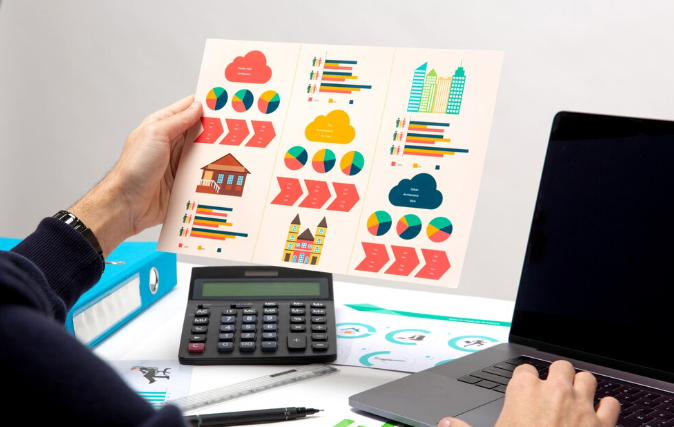 Person analyzing colorful business charts and graphs beside laptop and calculator.