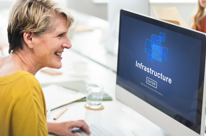 A woman smiling while using a computer with "Infrastructure" displayed on screen.