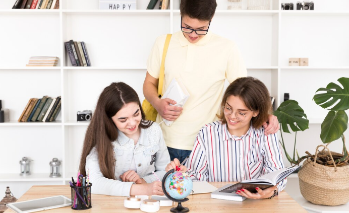 Three students studying together with globe and open book.