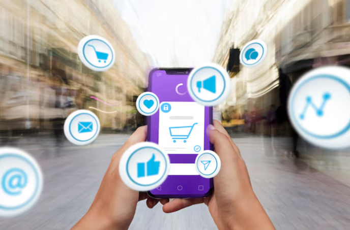 Hands holding a phone with shopping cart icons and digital marketing/social media symbols (represents mobile commerce).