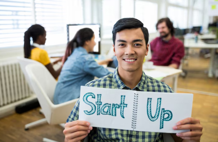 Young man proudly displaying handwritten startup sign in office.