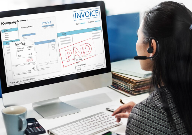 Woman reviewing a paid invoice on desktop computer with headset on.