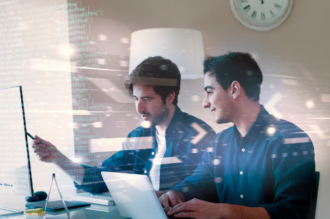 Two programmers working together on a project using laptop and screen.