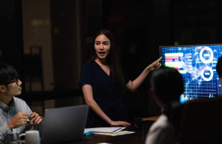 Businesswoman giving a presentation with data charts on screen.