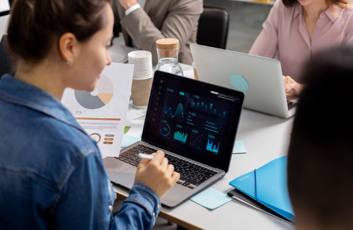 Woman analyzing data dashboards on laptop during office meeting.