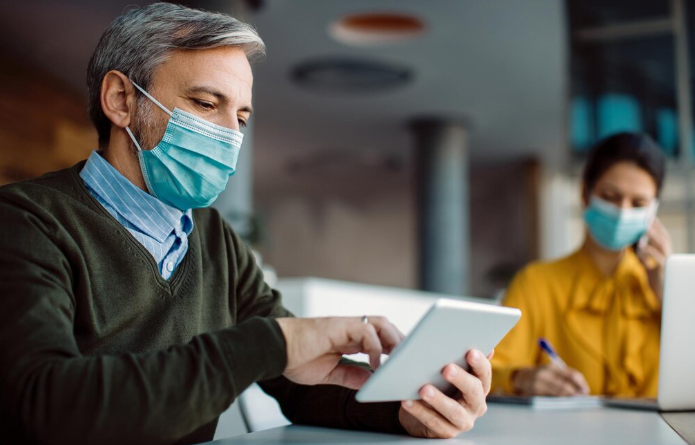 Man wearing face mask using digital tablet at workplace.