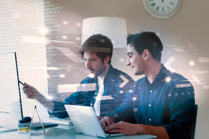 Two programmers working together on laptops with digital code overlay.