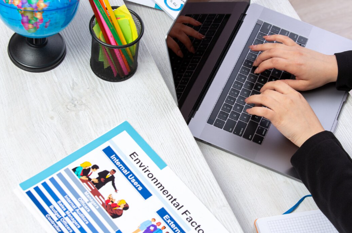 Close-up of a person working on a laptop with environmental factors document with Design Your Course.
